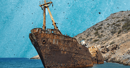 A rusty shipwreck sticking out of the water in front of a hill.
